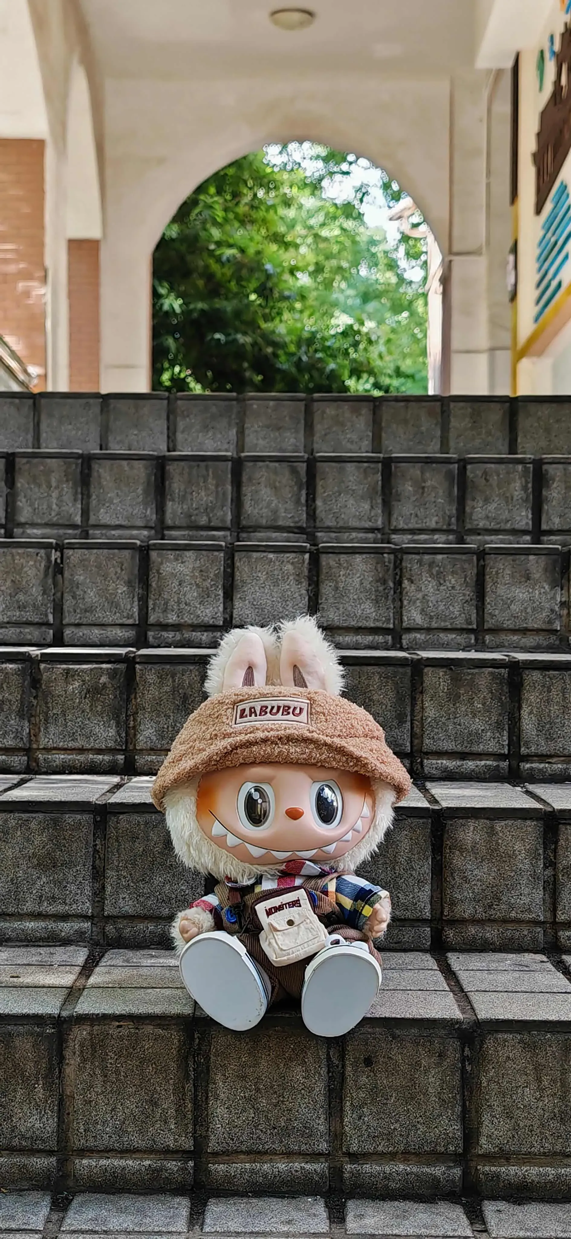 Cream white Labubu in patchwork outfit and hat on stone stairs outdoors