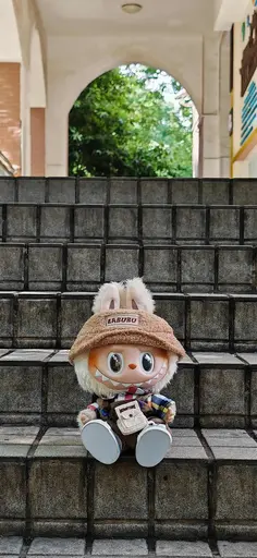 Cream white Labubu in patchwork outfit and hat on stone stairs outdoors